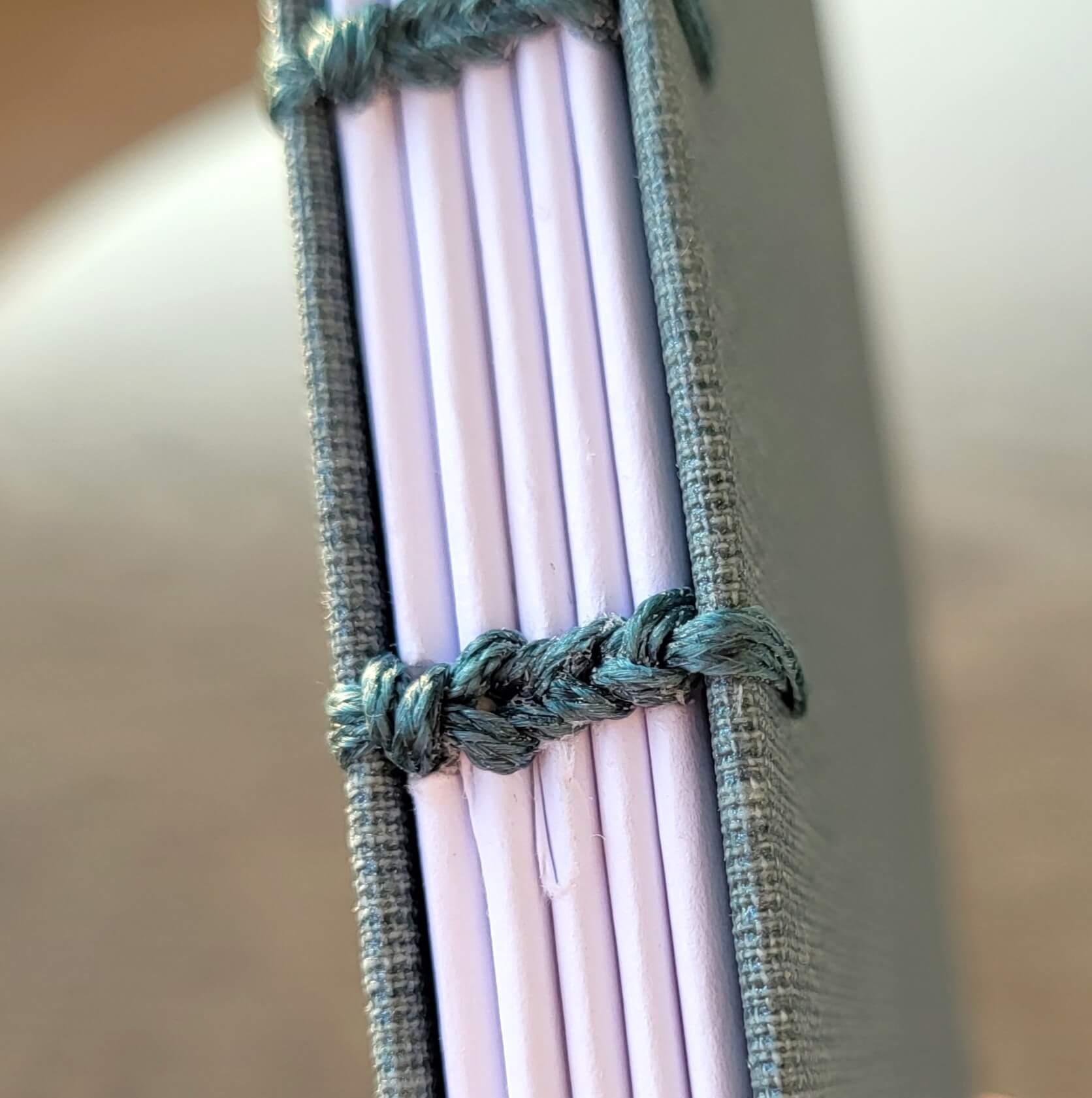 "Detailaufnahme der koptischen Buchbindung — sichtbare Kettenstichheftung mit grün-blauem Faden an hellviolettem Notizbuch aus dem Workshop München