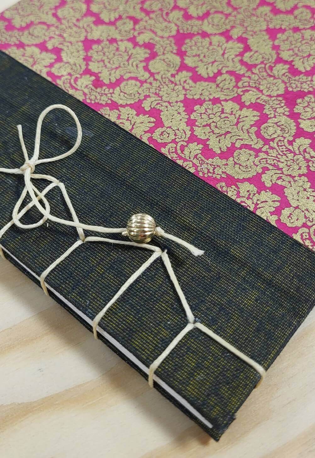 Handgebundenes Notizbuch aus dem Japanische Bindung Workshop München — dunkler Struktureinband mit pinkem Goldmusterpapier und dekorativer weißer Fadenheftung mit Perle
